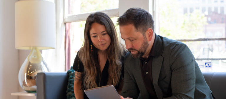 Adam and a client are looking at a tablet together in a well-lit room with modern decor.