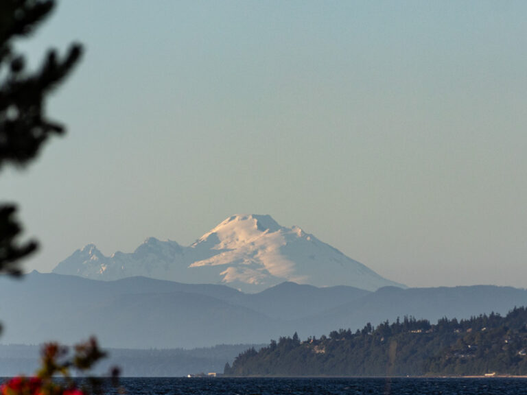 Towering snow-capped Mount Baker in the distance, a glowing street lamp in the foreground, and a tranquil Puget Sound.